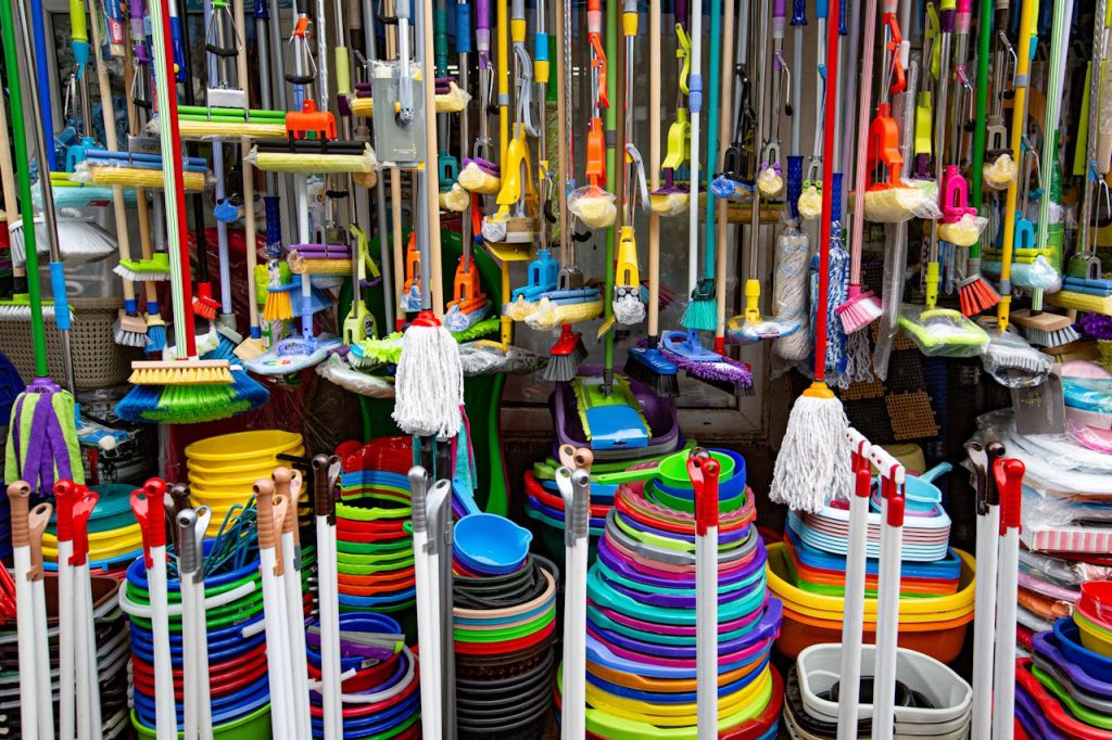 pexels-photo-6160302 Various colorful mops and brushes arranged with stack of plastic basins and bins in household goods supermarket